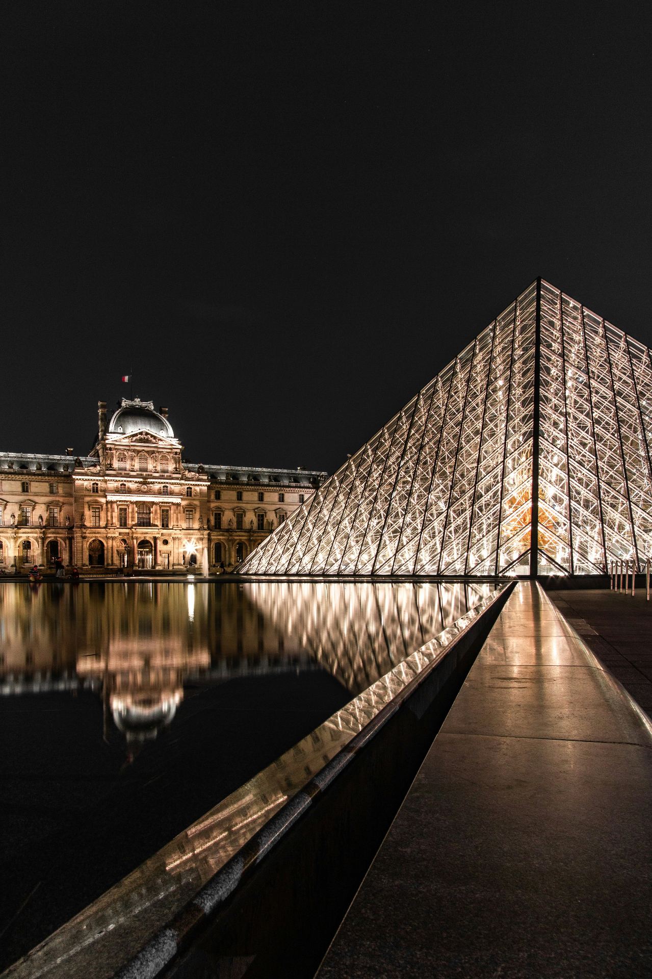 Pirâmide de vidro do Museu do Louvre iluminada à noite com reflexo na água