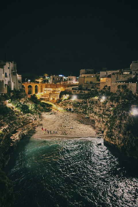 Polignano a Mare iluminada à noite, com a Lama Monachile e a ponte romana destacadas