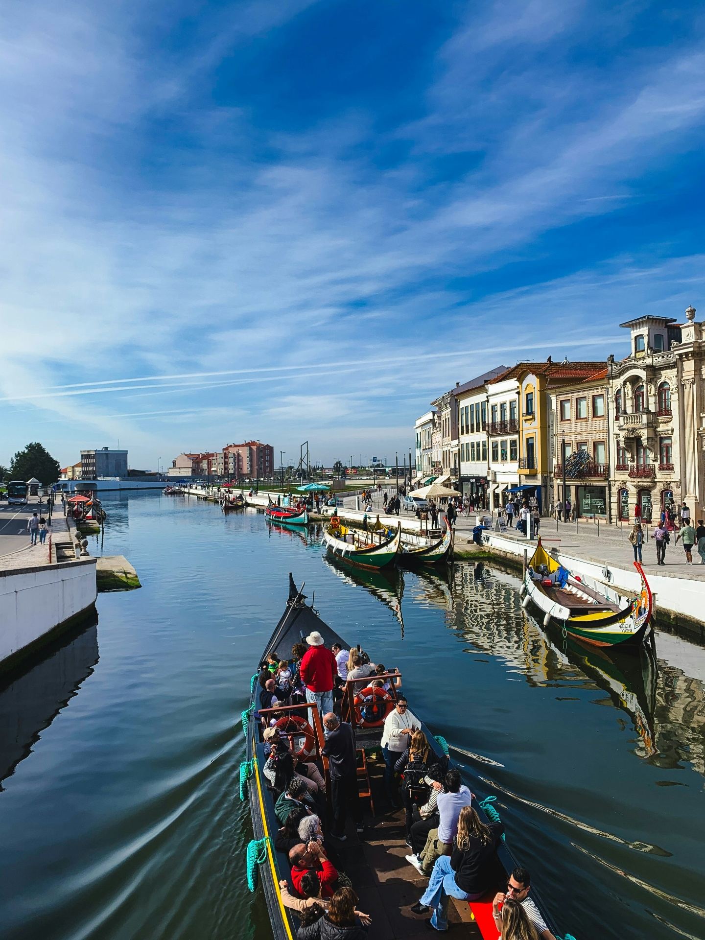 Barco moliceiro tradicional navegando pelos canais de Aveiro com turistas a bordo e edifícios Arte Nova ao fundo