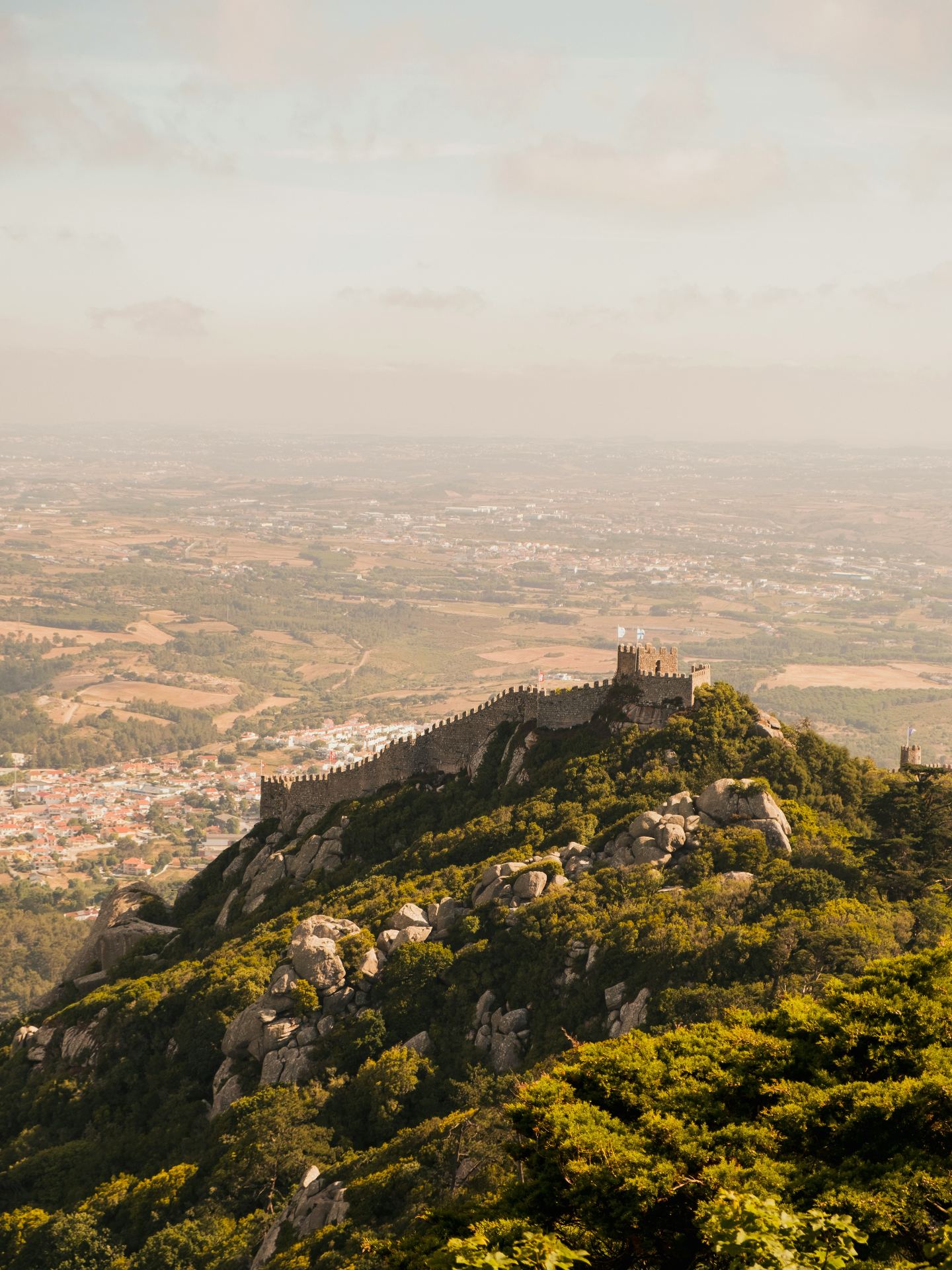 Vista aérea do Castelo dos Mouros com as suas muralhas serpenteando pela montanha e a planície de Sintra ao fundo