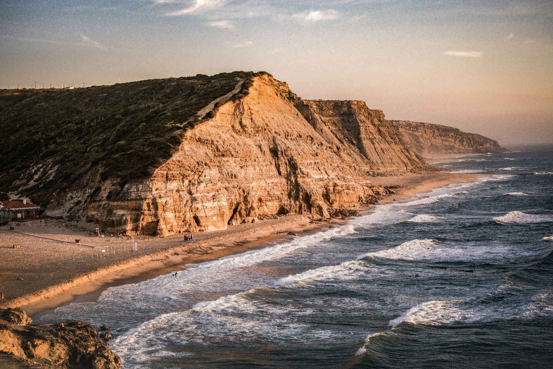 Praia da Ericeira ao pôr do sol com falésias douradas e ondas perfeitas para surf