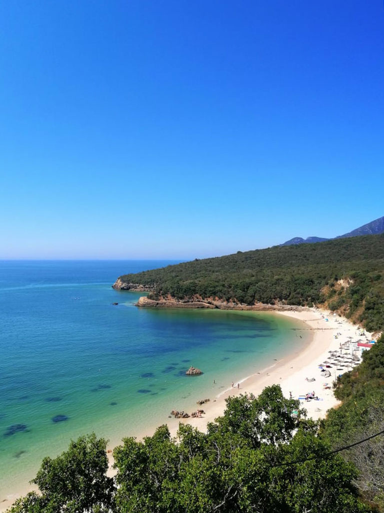 Praia de Galapinhos vista do alto com águas turquesa cristalinas, areal branco e encosta verdejante da Serra da Arrábida