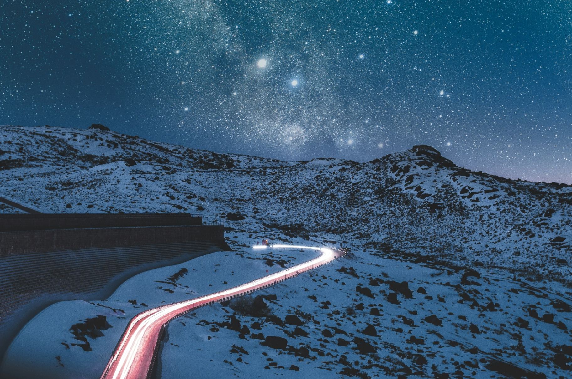 Serra da Estrela nevada à noite com estrada iluminada pelas luzes de carros e Via Láctea no céu estrelado