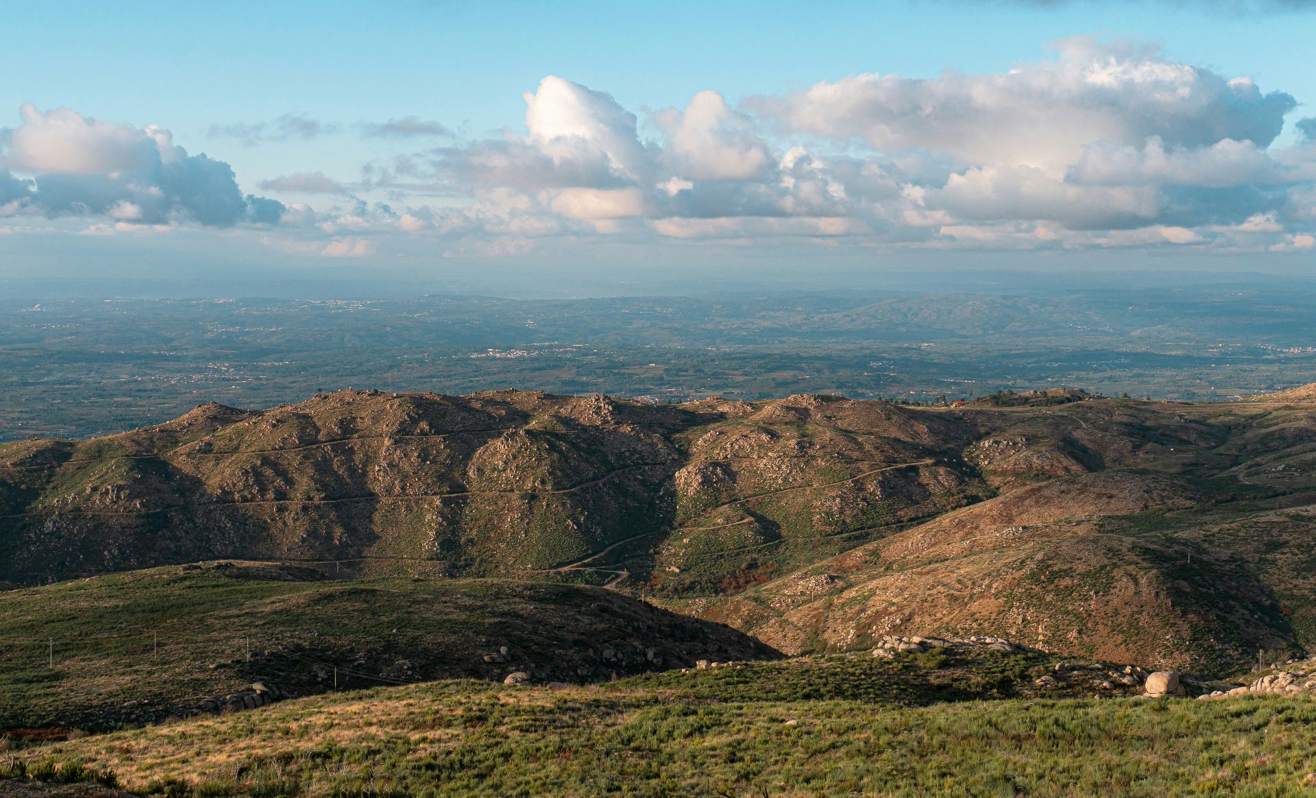Vista panorâmica da Serra da Estrela com montanhas ondulantes, vegetação rasteira e nuvens dramáticas