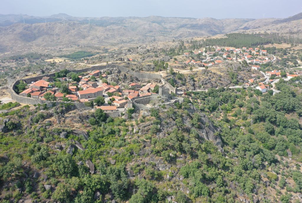 Vista aérea da aldeia histórica de Sortelha com muralhas medievais e casas de pedra no topo de uma colina rochosa