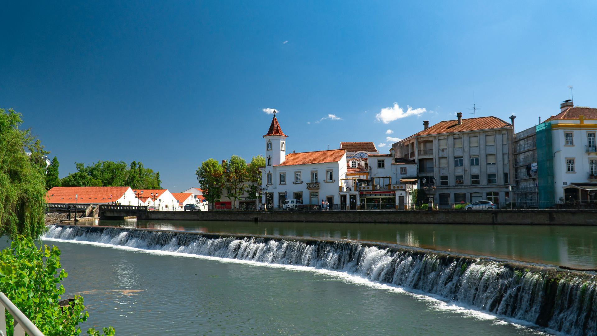 Vista do centro histórico de Tomar com o Rio Nabão, açude e casas tradicionais portuguesas com torre sineira